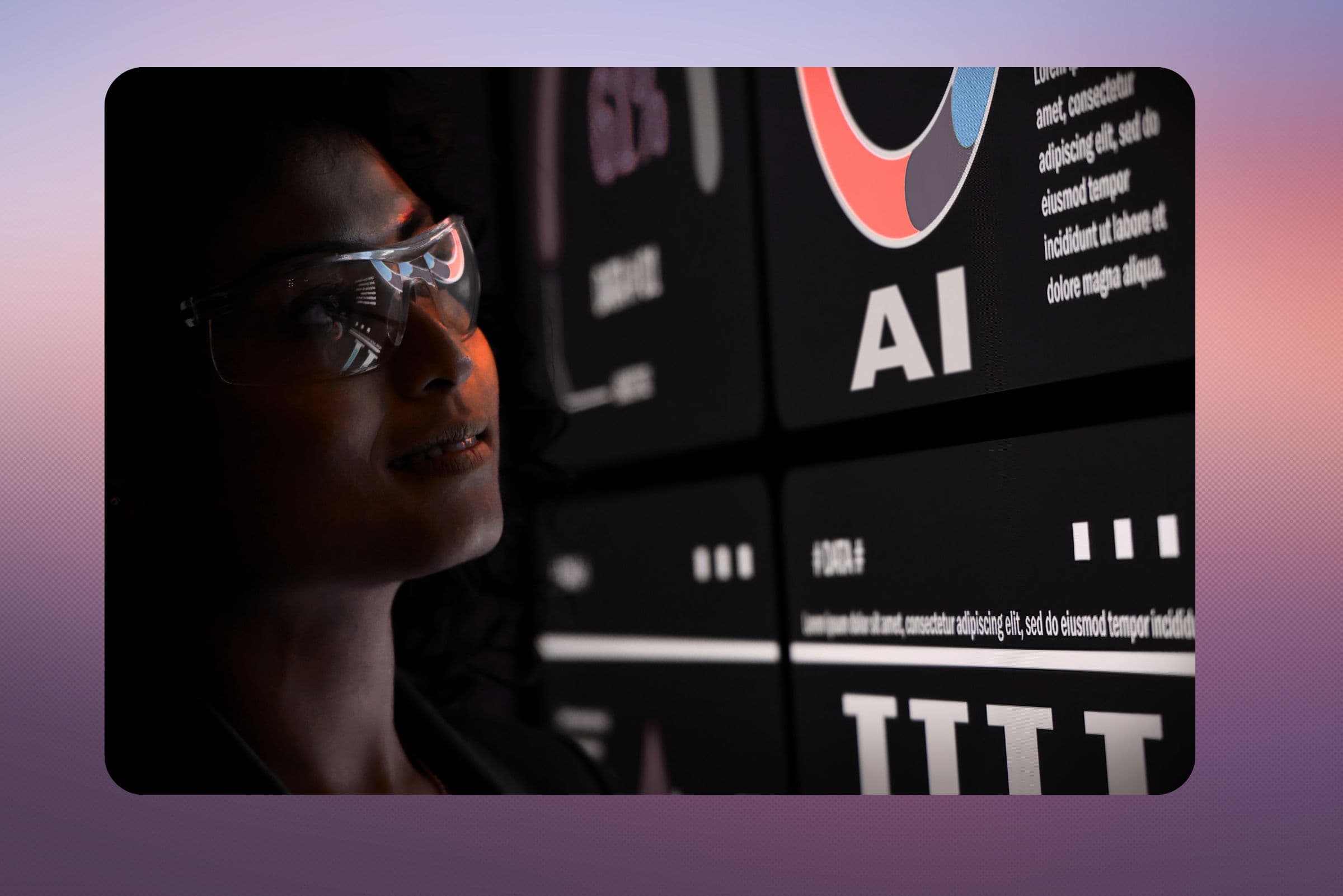 A woman in glasses lit by a wall of screens showing AI