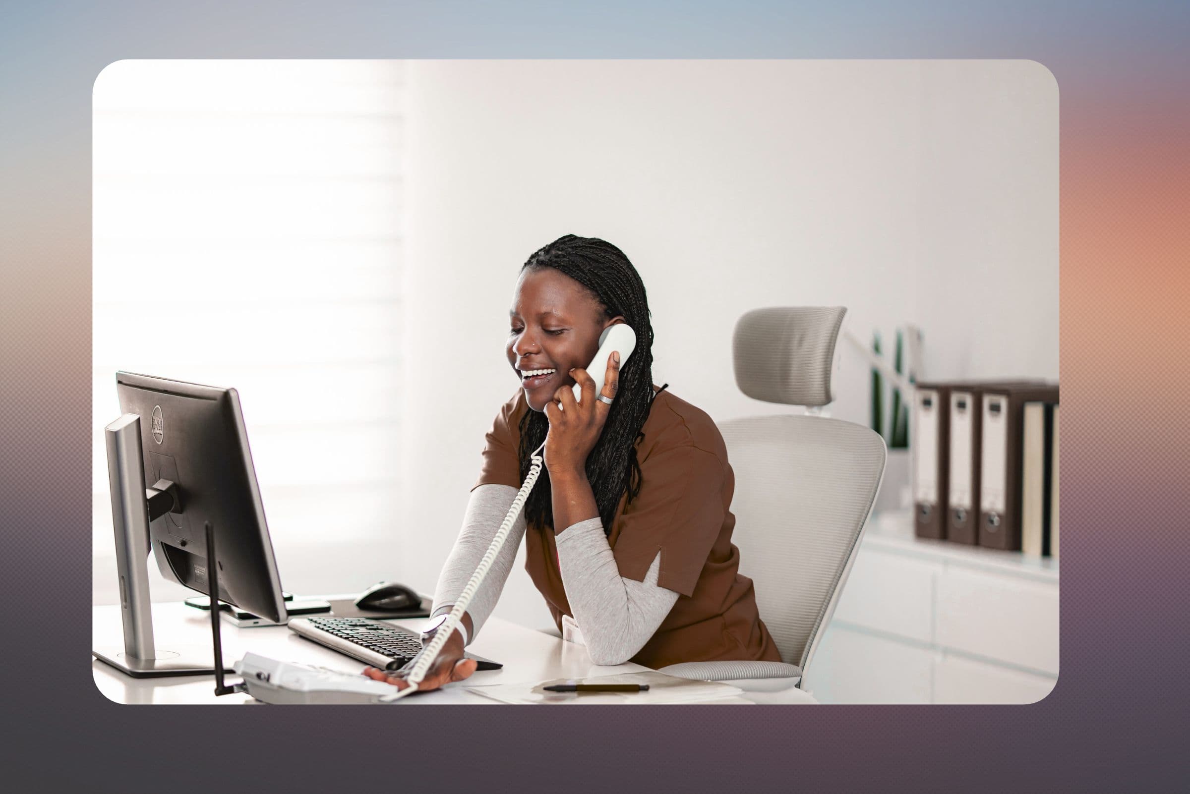 A receptionist smiling on the desk phone at a bright office desk